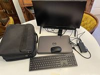 Setup showing all items: Dell laptop, monitor, wireless keyboard, mouse, carrying case, and charger cables on table.