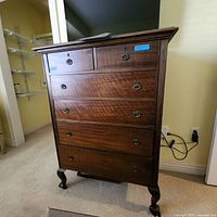Full front view of the tall wooden dresser showing five drawers with decorative handles and curved legs.
