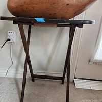 Wooden TV tray shown standing on carpet near white wall and electrical outlet, with wooden goose figurine on top.
