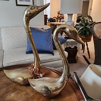 Pair of brass geese sculptures displayed on a wooden table in a living room setting.