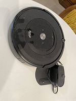Top view of iRobot Roomba vacuum cleaner with attached charging dock on a white surface showing black exterior and silver button.