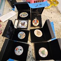 Overview of all seven artist signed pins in black display boxes on a counter.