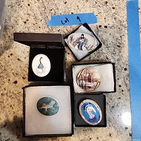 Top-down view of five collectible artist signed pins in individual boxes on a granite countertop, visible detailed artwork for each pin including animals and figures.