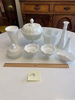 All nine vintage milk glass hobnail pieces on a table with ruler for scale, including vases, jars, bowls, and lidded jar with finial.