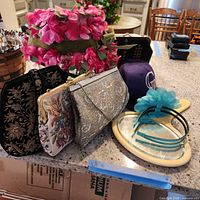 Full view of vintage hat, three hand purses, purple cap, blue headbands on oval mirror, and decorative glass jar on countertop