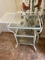 Full view of white metal and glass rolling hospital cart with two shelves and caster wheels.