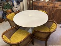 Photo showing round white tabletop and four mustard yellow upholstered vintage chairs around it in a room.