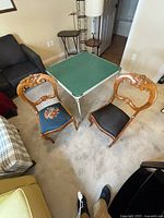 Two antique wooden dining chairs with carved backs, one with floral fabric seat and one with black fabric seat, placed next to the card table on carpet.