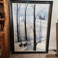Framed winter landscape painting showing bare trees, snow, geese, a stream and building in the distance.