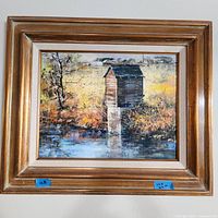 Photo of the framed oil painting showing a rustic wooden structure by a river in autumn, signed by D. Payton at bottom right.