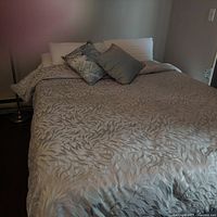 Queen size bedspread with beige and grey leafy textured pattern on bed with decorative pillows