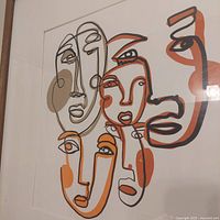 Close-up of abstract face art print with overlapping faces in orange, beige, and brown tones.