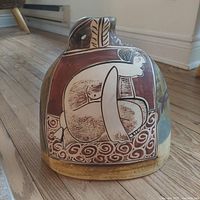 Side view of ceramic vase showing stylized human figure design in earthy colors with detailed patterns around the base.