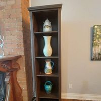 Full bookshelf showing four shelves and top shelf with four decorative ceramic pitchers and vases