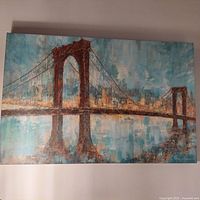 Canvas print of a brown suspension bridge with city skyline in background and water reflection below