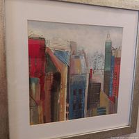 Front view of the framed colorful cityscape sketch with a white mat and silver frame showing multiple buildings with artistic paint and line work.