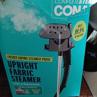 Close-up photo of retail box showing Conair CompleteSteam Upright Fabric Steamer with claims of 1200 watts, energy-saving steamed pause, and kills 99.9% of bacteria.