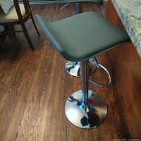 Two gray adjustable bar stools side by side at kitchen counter, showing seat and chrome base with footrest.