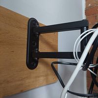 Close-up photo of black metal TV mount arm attached to wood panel on wall, showing dual pivot joints and mounting screws.