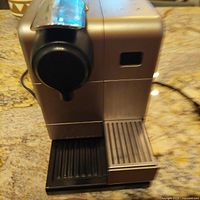 Front and side view of silver Nespresso coffee machine on kitchen countertop showing capsule lever and drip tray.