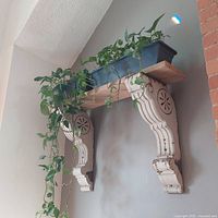 Side angle photo showing corbels mounted on the wall supporting a wooden shelf with a planter on top.