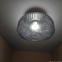 Close-up image of one installed round ribbed glass ceiling light fixture illuminated, showcasing glass texture and lighting effect.