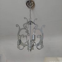 Front angle photo of silver metal chandelier with three candle-style lights and decorative scrollwork, hanging from adjustable chain.