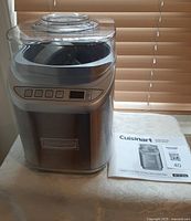 Front view of the stainless steel Cuisinart ice cream maker with control panel and manual beside it.