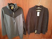 Two tops and one jacket hanging on hangers against wooden door. Left is Indyeva black pullover top with zipper and high collar, center is Eileen Fisher textured black open front jacket, and right is Eileen Fisher textured top slightly visible underneath jacket.