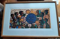 Framed print featuring colorful stylized Indigenous figures and symbols in wood frame with white mat.