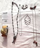 Overview of all jewelry items laid out on white cloth: watch face bracelet, long beaded necklace, layered geometric hoops, pussy willow pierced earrings, cranberry pearl and bead necklace
