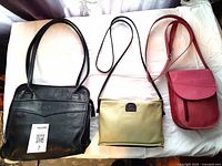 Three leather purses displayed side by side on a white surface: large black handbag with dual handles, small lime green purse, and small pink purse with shoulder strap.