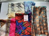 Photo showing five silk scarves folded and laid out, displaying various colors and patterns including elephants, floral designs, and tie-dye.