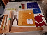 Overview of various stained glass sheets and pieces in yellow, blue, red, green, and orange colors, along with the glass cutter tool, snapping tool, and pliers.