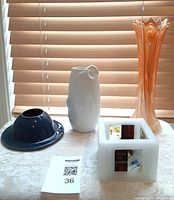 Four vases and one square artisan candle holder on a table with a window background