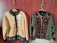 Front view of cream and green sweater jackets hanging side by side