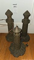 Three cast iron lighthouse-shaped lamps grouped on wooden floor