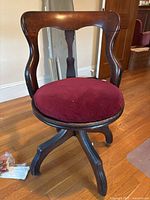 Front view of antique wooden swivel chair showing curved backrest and burgundy upholstered padded round seat.