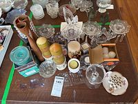 Top-down photo showing assortment of ceramic, glass, and crystal candle holders, candles, including two large green and orange pillar candles on white ceramic holders, smaller votive holders, and boxed candle.