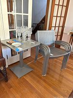 View of metal table with glasses on top, one stackable metal chair next to it.