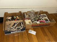 Two boxes filled with assorted vintage and artisan costume jewelry pieces including necklaces, brooches, and accessory sets.