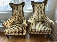 Front view of two mid-century throne style chairs next to window. Chairs have tufted backs, wide armrests and striped upholstery in shades of brown and cream.
