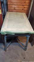 Full view of the dining table showing the enamelware top with pale green border, spindle legs, and wooden base.