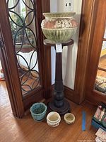 Full view of four planters arranged around wooden pedestal plant stand in a corner of a room.