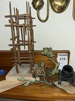 Photo showing wooden skyscraper sculpture, metal candle holder resembling plant branches with bird, military mortar replica, and historical paper.