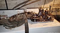 Silverplated tea service and vintage hammered aluminum platters displayed on laundry appliances in basement setting.