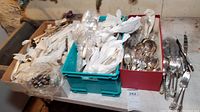 Three bins and loose pieces of mixed silver-plated flatware on concrete floor