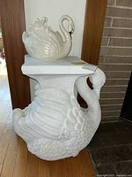 White swan plant stand sculpture with detailed feathers, holding a flat surface on top for plants