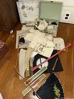 Assortment of vintage handkerchiefs, fans, shoe horn, and back scratcher arranged on wooden floor.