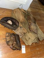 Overview of all items: leather shooting jacket, catches mitt, baseball glove, and baseball on wooden floor